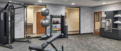A gym with exercise equipment, a bench, and a rack of sports balls.
