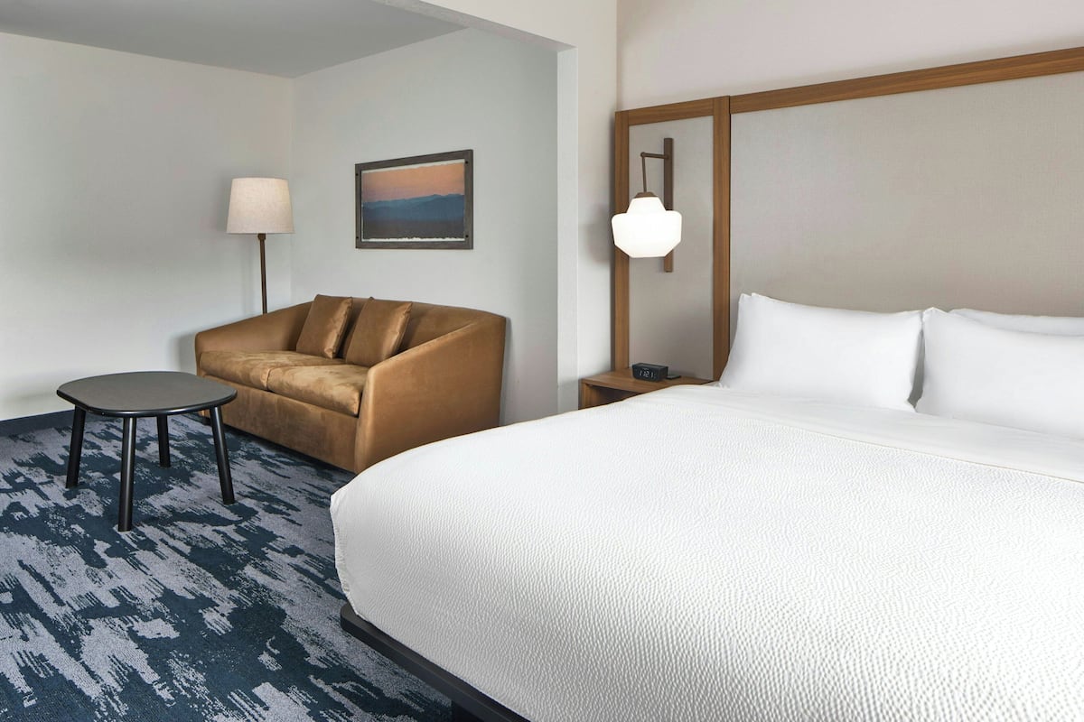 Une chambre d’hôtel avec un lit, un canapé, une petite table, une lampe et un tableau au mur.