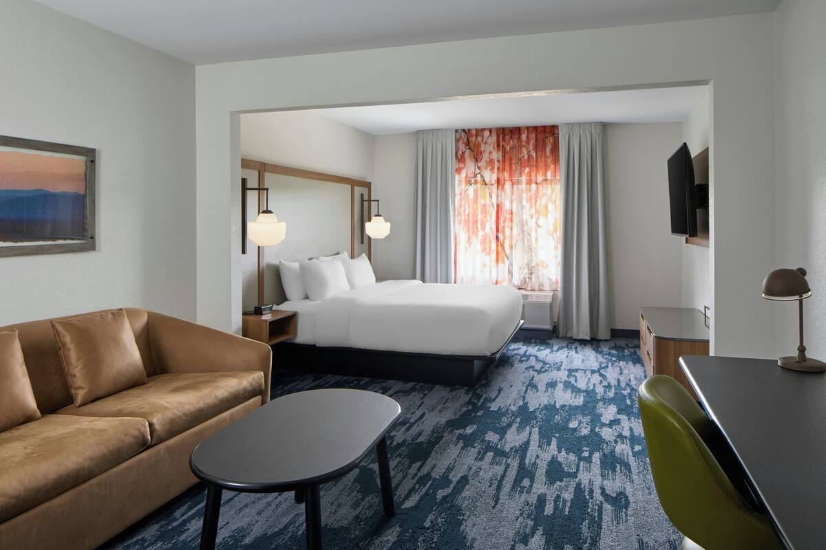 Une chambre d’hôtel avec un lit, un canapé, un bureau, une chaise, une télévision et un tableau au mur.