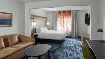 Habitación de hotel con cama, sofá, escritorio, silla, televisor y un cuadro en la pared.