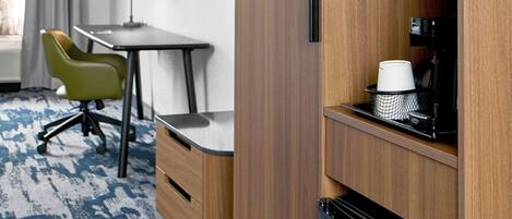 A compact hotel room with a kitchenette, a desk, a chair, a television, and a window with curtains.