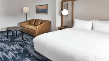 Habitación de hotel con cama, sofá, mesita, lámpara y un cuadro en la pared.