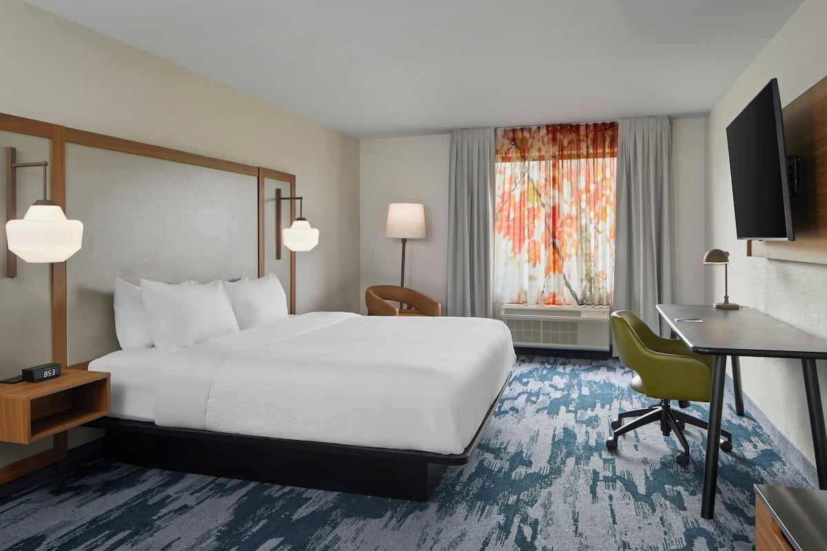 Une chambre d’hôtel équipée d’un lit, d’un bureau, d’une chaise, d’une télévision, d’une lampe et d’une fenêtre avec des rideaux.