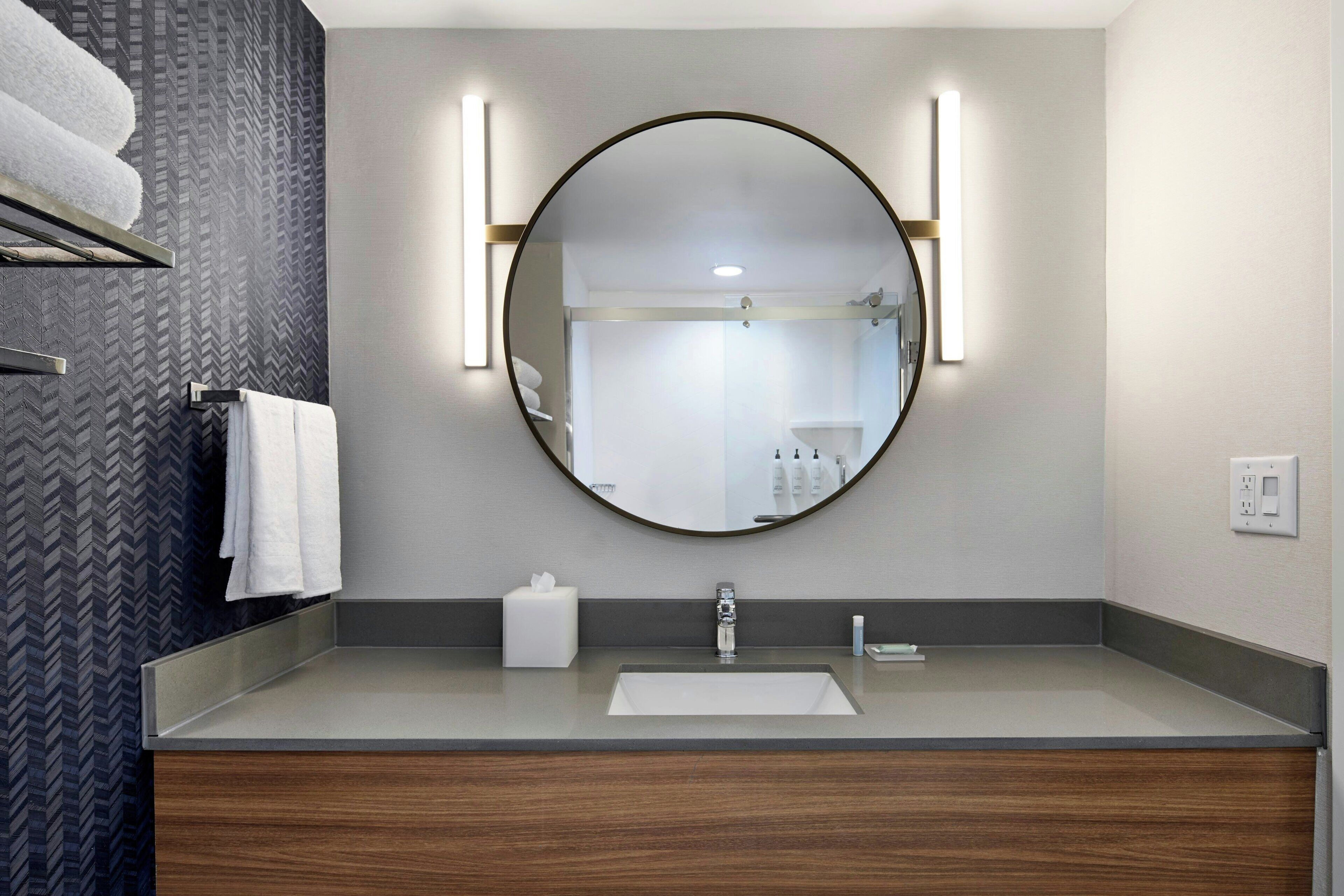 A modern bathroom with a round mirror, a sink, and a towel rack.