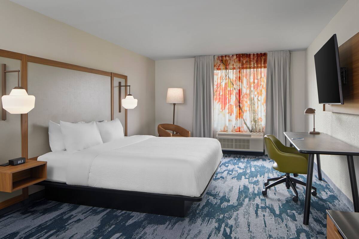 Une chambre d’hôtel avec un grand lit, un bureau, une chaise, une télévision et une fenêtre avec des rideaux.