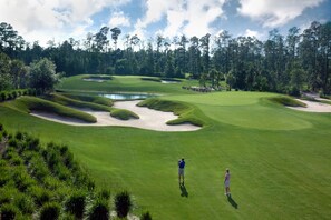 Un campo de golf con búnkeres de arena, un estanque y altos árboles al fondo.