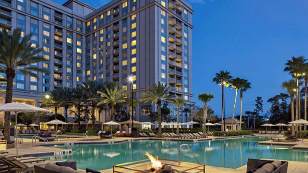 A hotel with a swimming pool, lounge chairs, and palm trees.