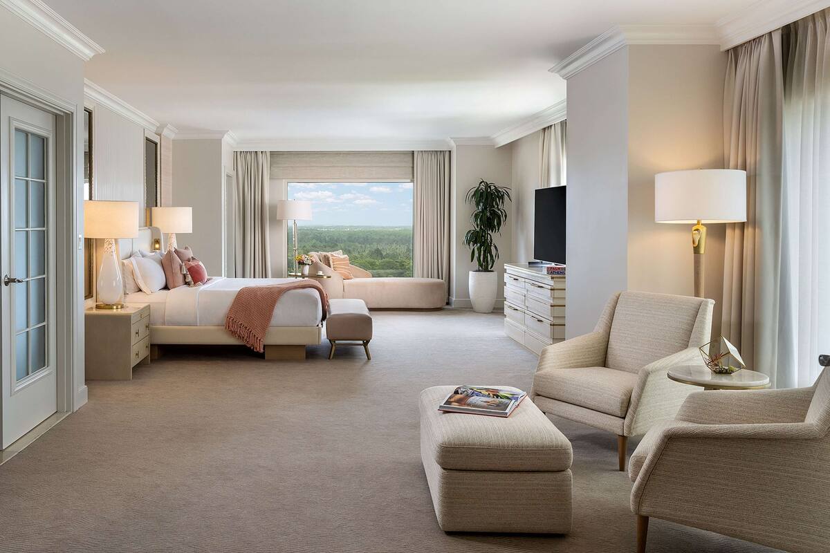 Une chambre d’hôtel spacieuse, dotée d’un grand lit, de deux fauteuils, d’un canapé, d’une télévision et offrant une vue sur l’extérieur.