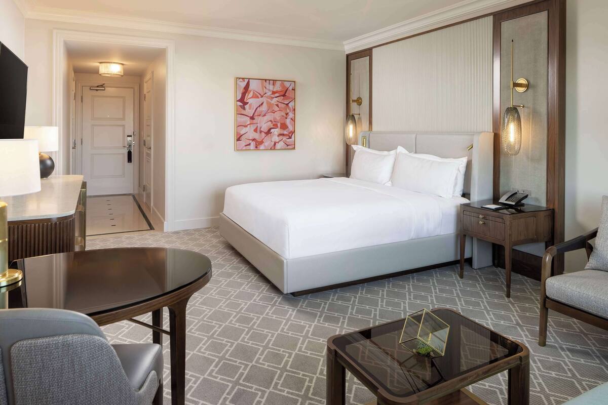 Une chambre d’hôtel avec un grand lit, un bureau, une chaise, une petite table et un téléphone fixé au mur.