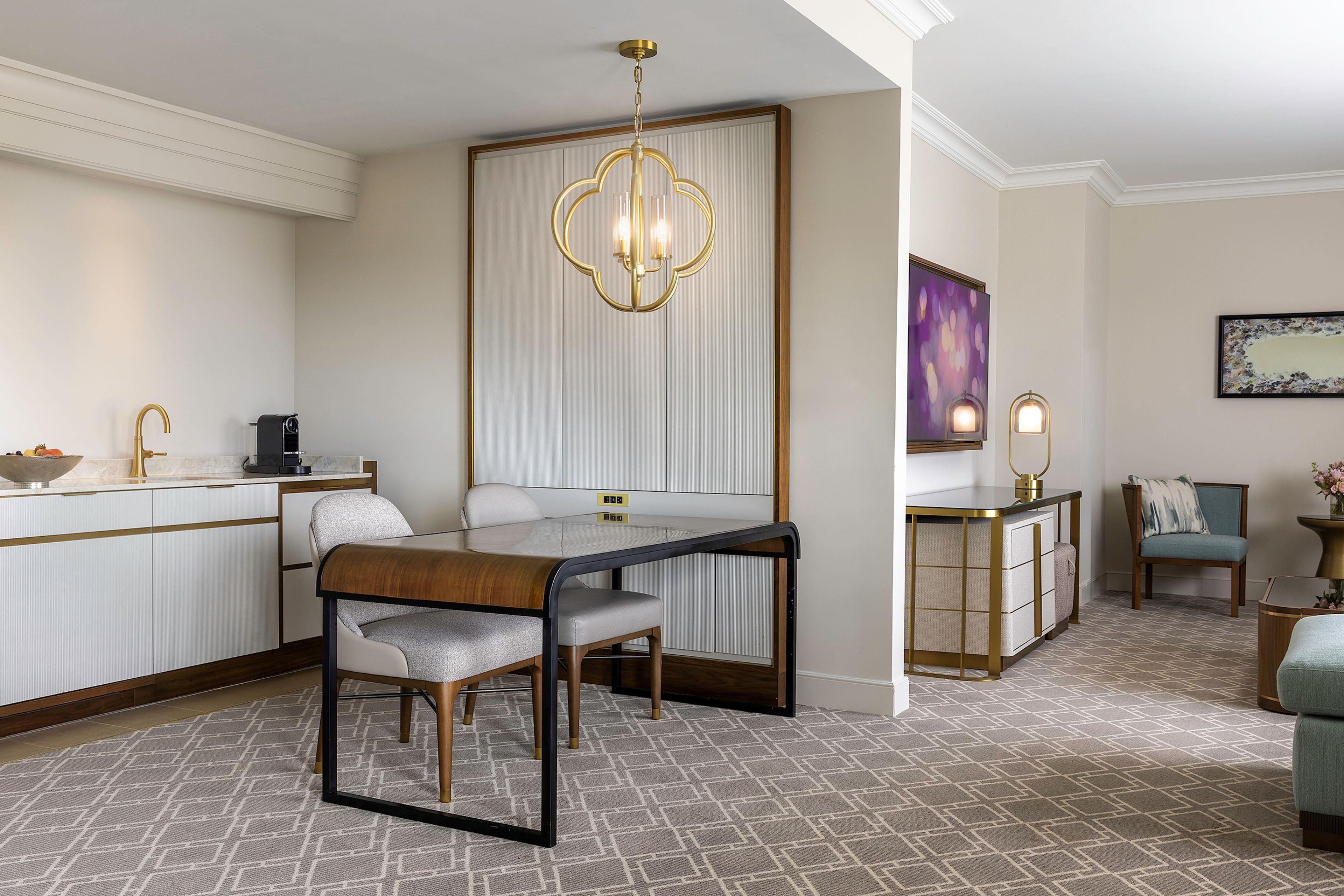 A modern hotel room with a dining area, a sofa, a side table, and a decorative wall piece.