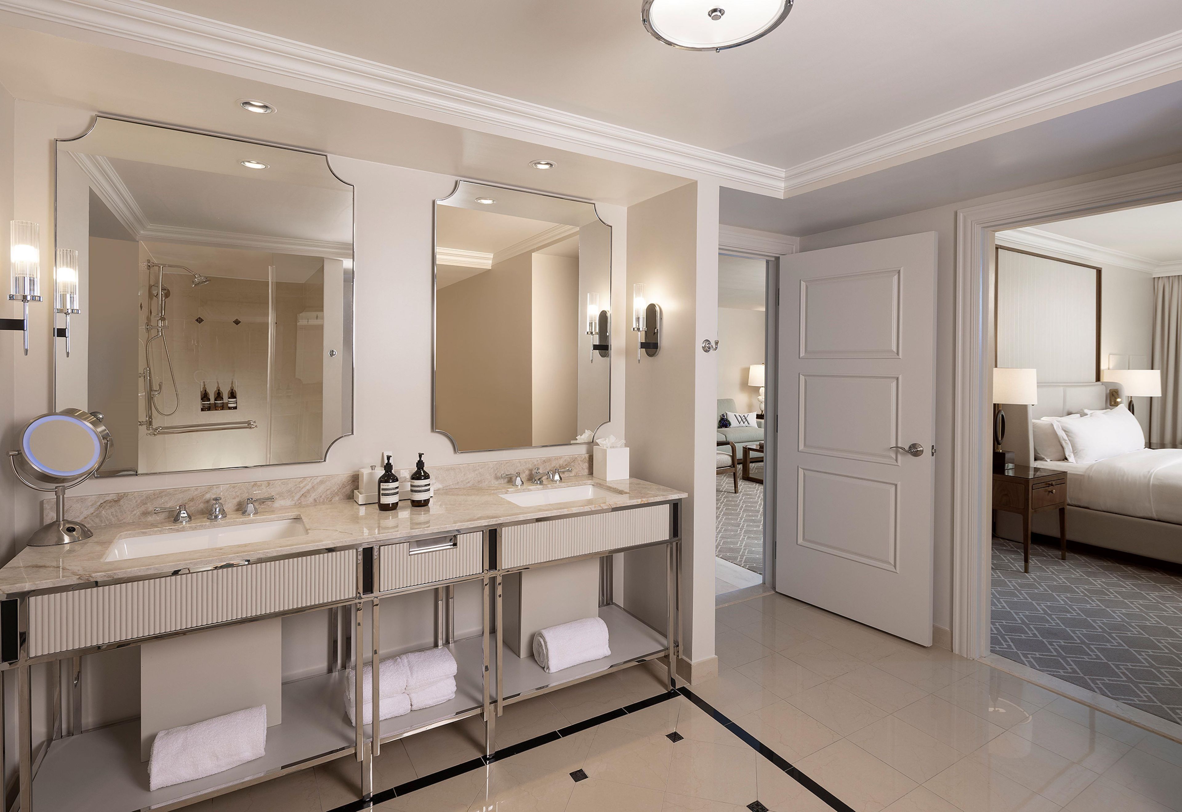 A hotel bathroom with a double sink, a large mirror, a shower, and a towel rack.
