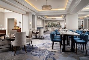 A spacious hotel dining area with multiple tables and chairs, a central bar area, and a view into the kitchen. - Waldorf Astoria Orlando - An Official Walt Disney World® Hotel (Orlando)