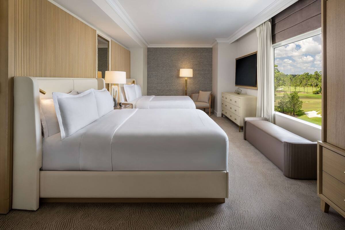 Une chambre d’hôtel avec un grand lit, un bureau, une chaise, une télévision et une fenêtre donnant sur un terrain de golf.