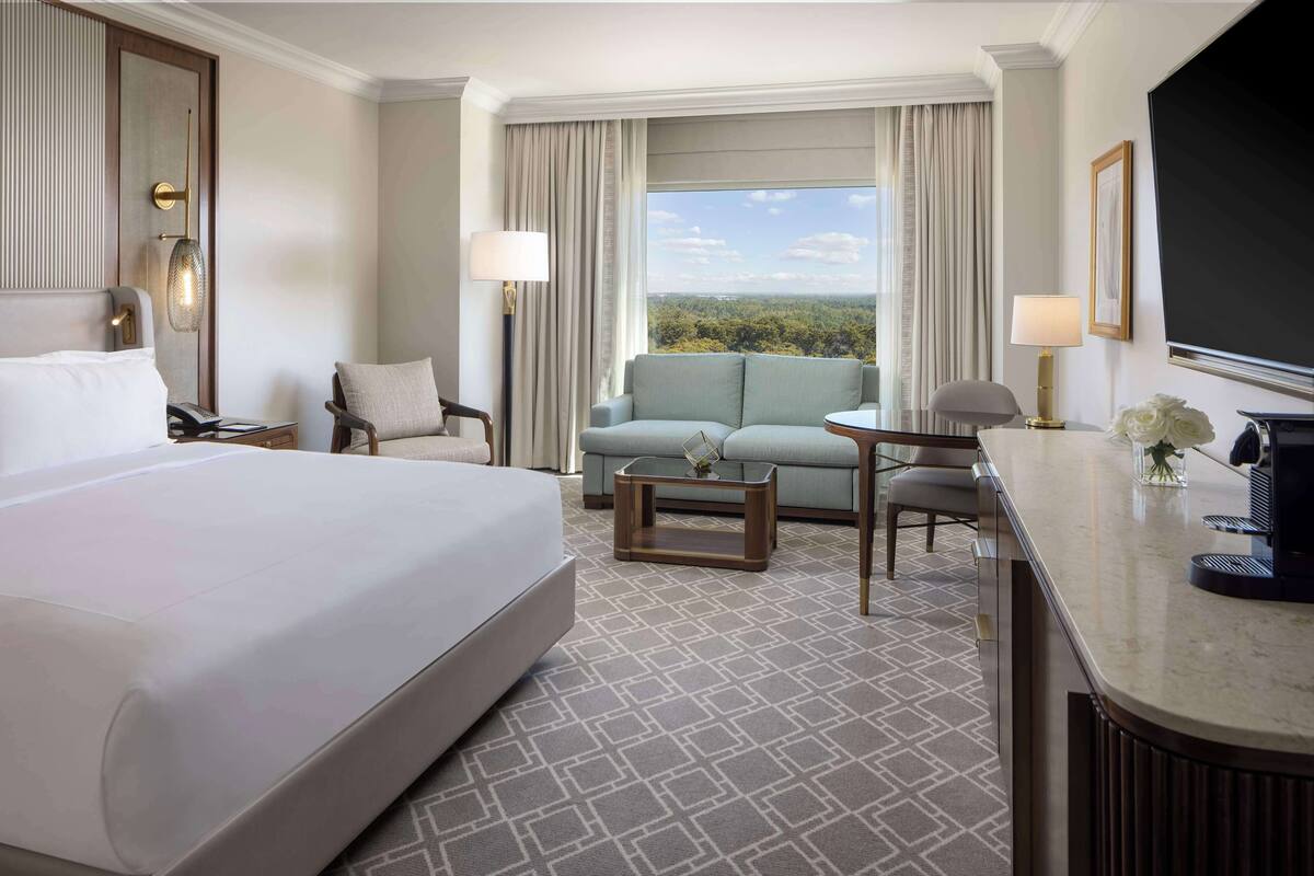 Une chambre d’hôtel avec un grand lit, un canapé, une petite table, un bureau et un téléviseur.