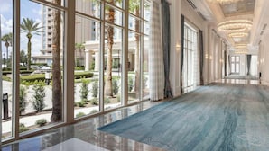 Un vaste couloir d’hôtel, doté de grandes fenêtres, d’un tapis bleu et d’élégants lustres.