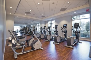 Un gimnasio con varias máquinas de ejercicio, ventanas amplias y suelo de madera.