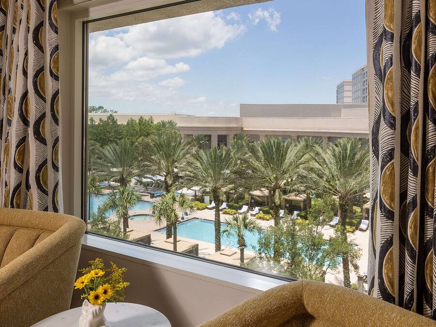 Quarto de hotel com vista para a área da piscina, incluindo palmeiras e espreguiçadeiras.