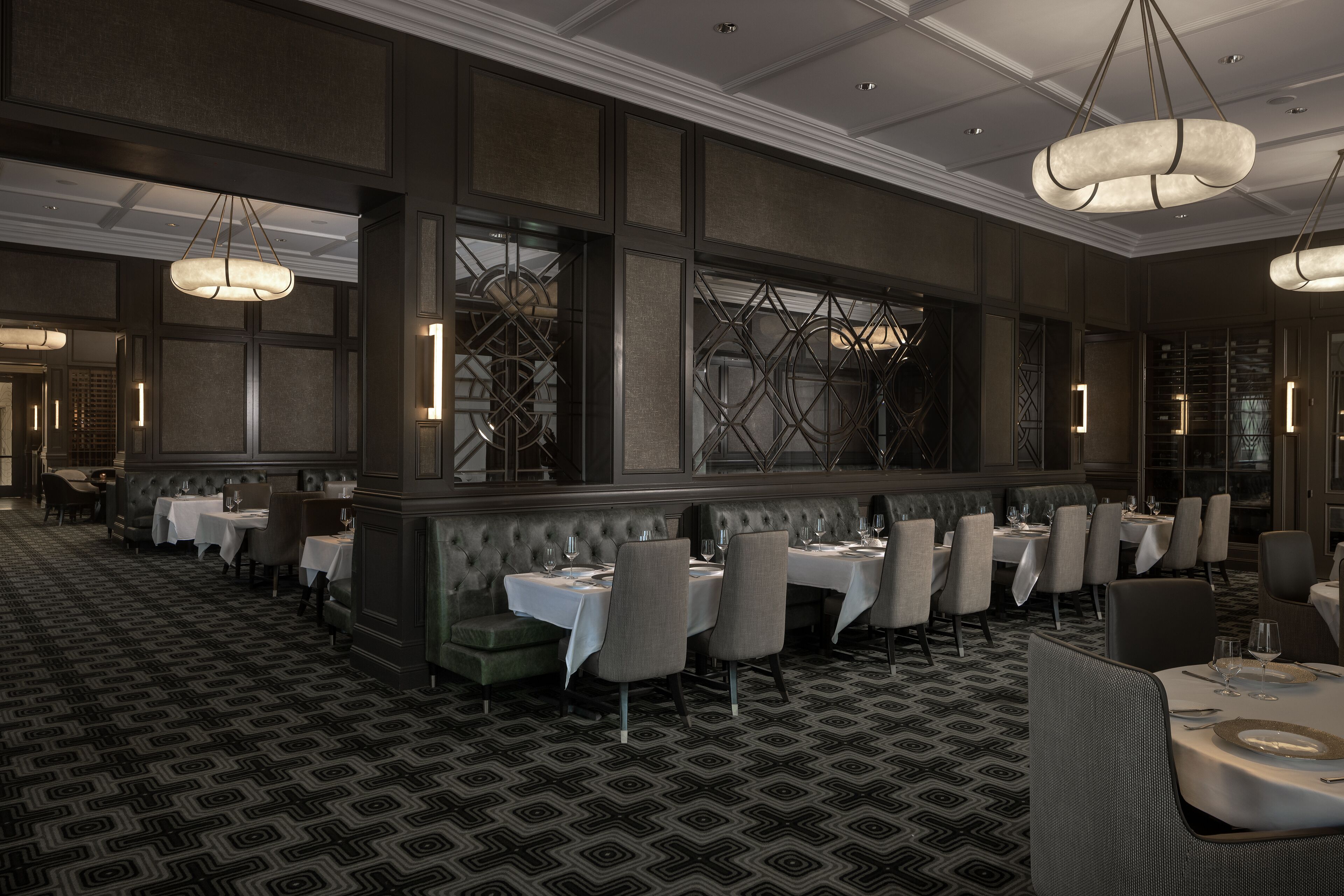 A formal dining area with multiple tables and chairs, a patterned carpet, and a modern chandelier.