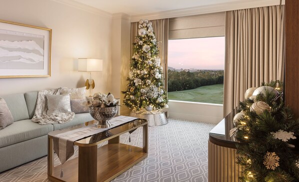 Una sala de estar moderna con un árbol de Navidad, un sofá, una mesa de centro y un amplio ventanal con vistas a un paisaje verde.