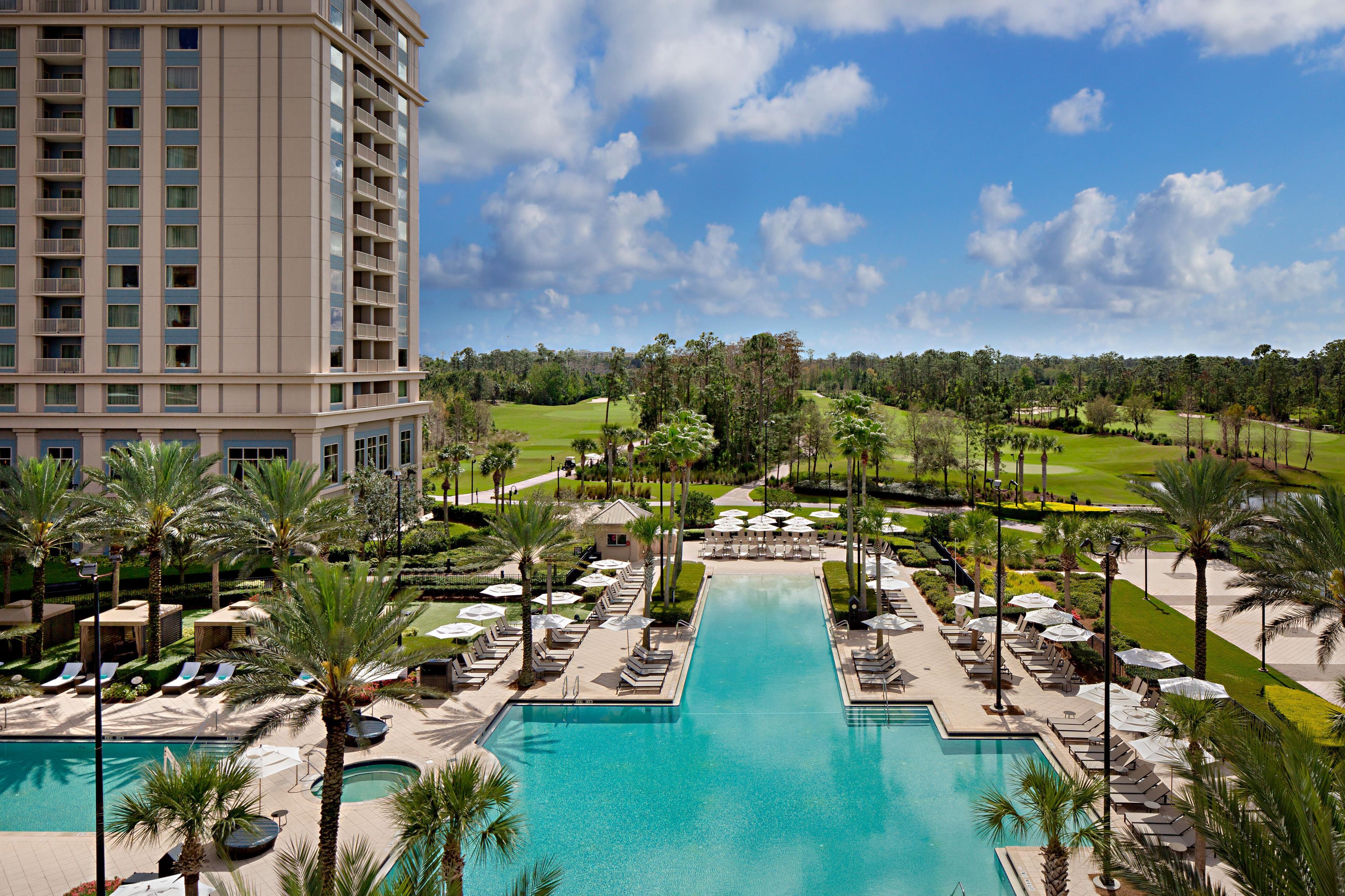 A hotel with a swimming pool, sun loungers, and a golf course in the background.
