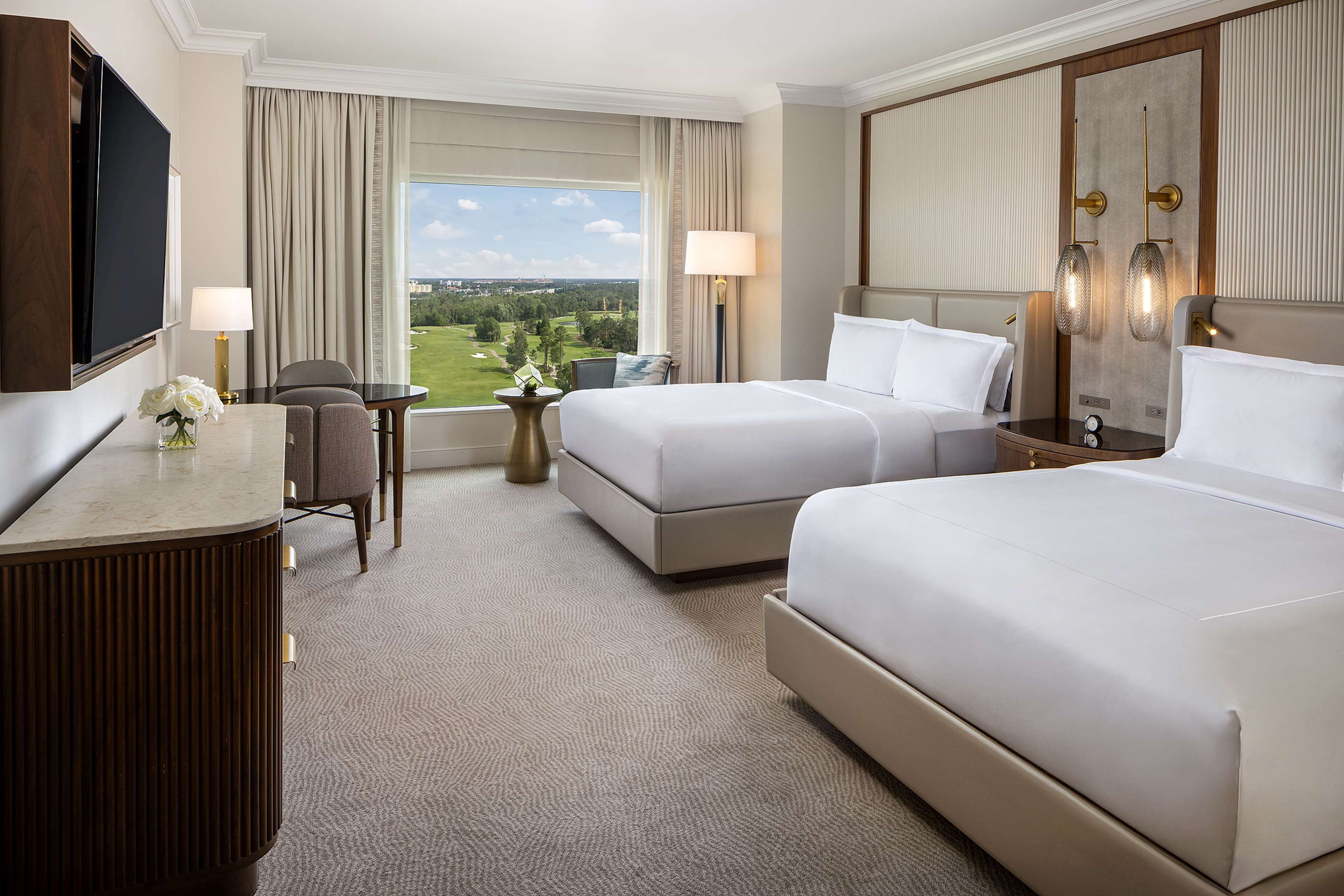 Habitación de hotel con dos camas, un escritorio, una silla, un televisor y vistas al exterior.
