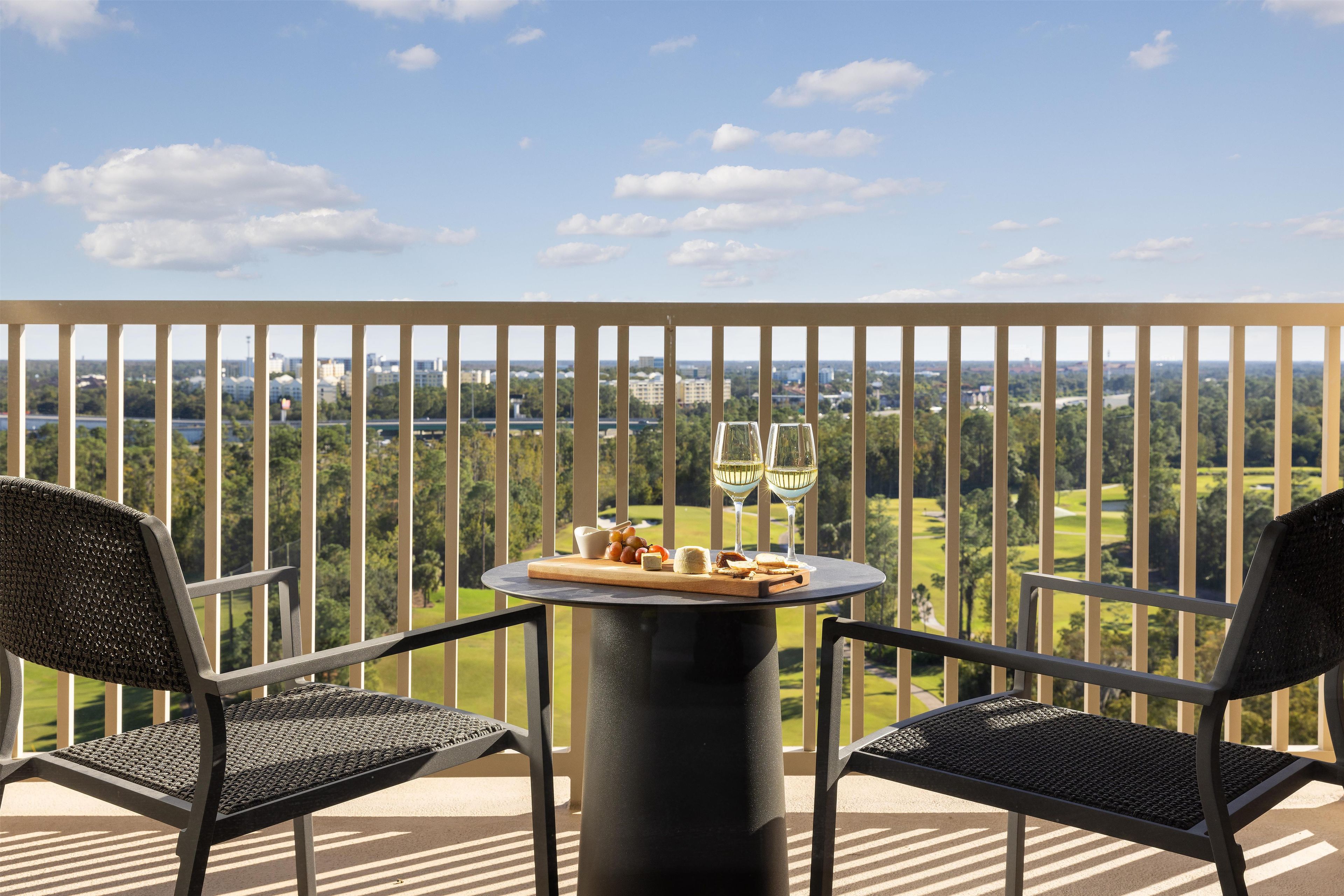 Un balcon avec deux chaises, une table avec une bouteille de vin, des verres et un petit panier de fruits.