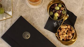 A table with a black folder, a bowl of olives, a bowl of nuts, and a glass of drink.