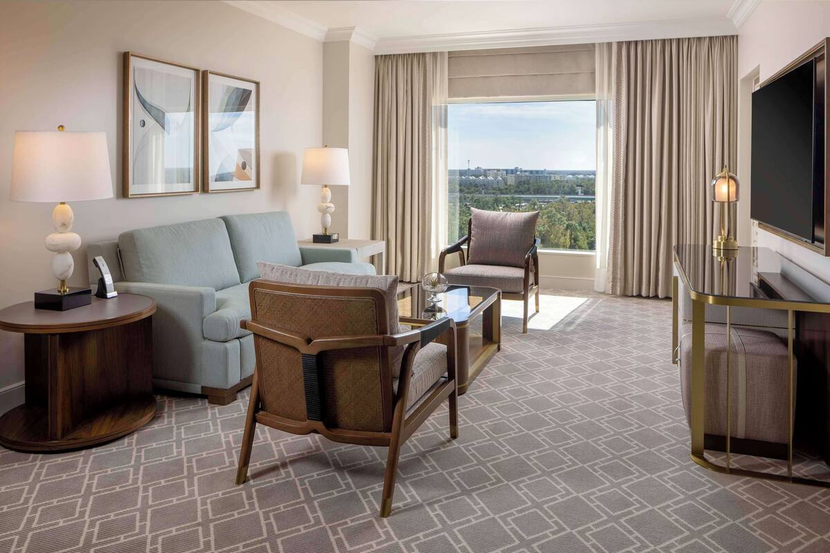 Une chambre d’hôtel avec un canapé, des fauteuils, une table basse, une télévision et une vue sur la ville.