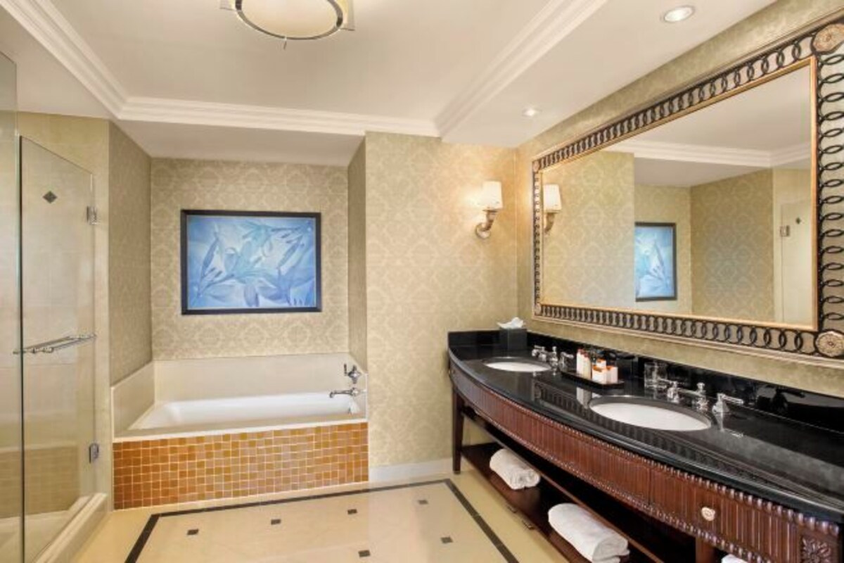 A bathroom with a large mirror, a bathtub, and two sinks.