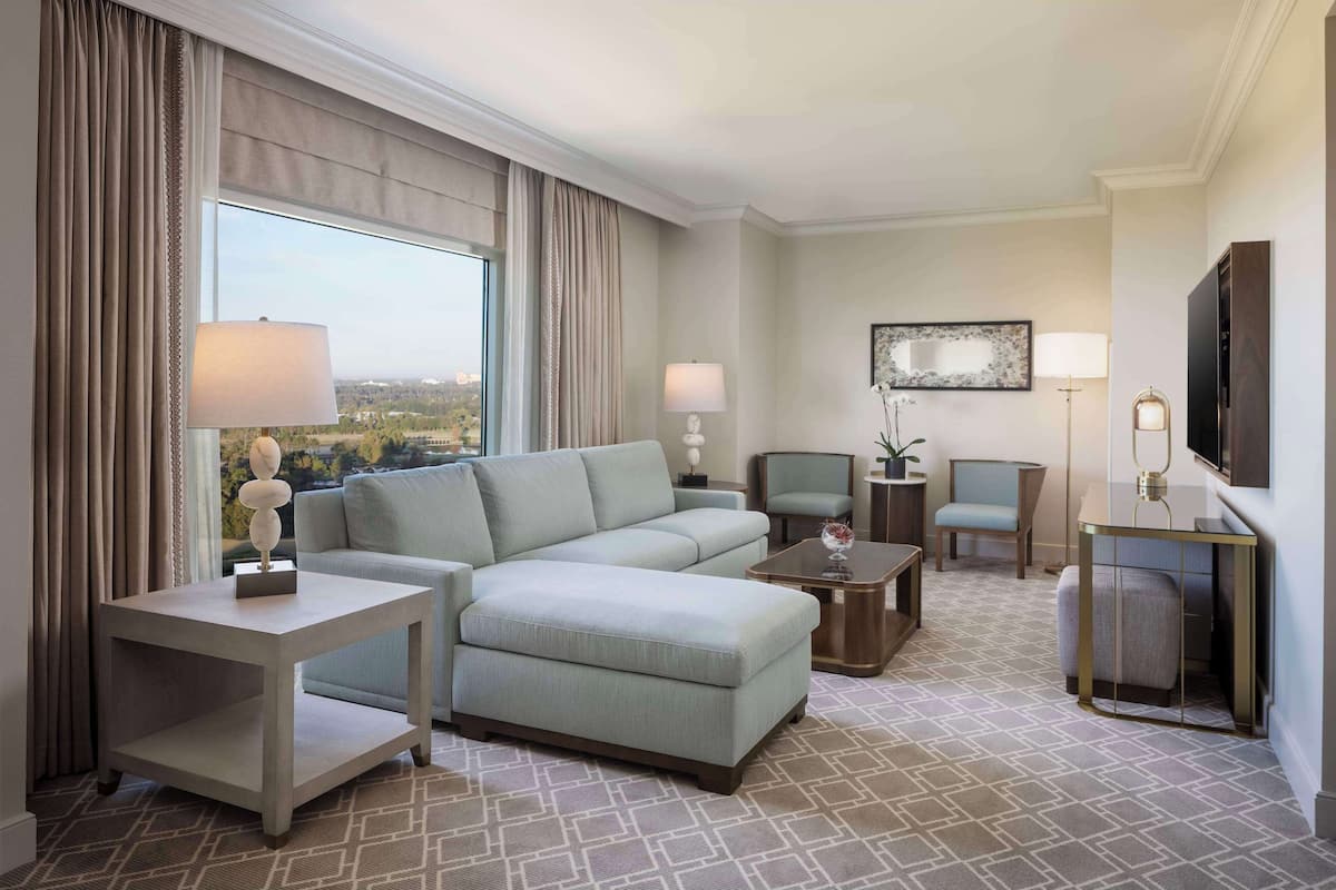 Une chambre d’hôtel moderne, dotée d’un canapé d’angle, d’une petite table, d’une chaise, d’un téléviseur et d’une grande fenêtre avec des rideaux.