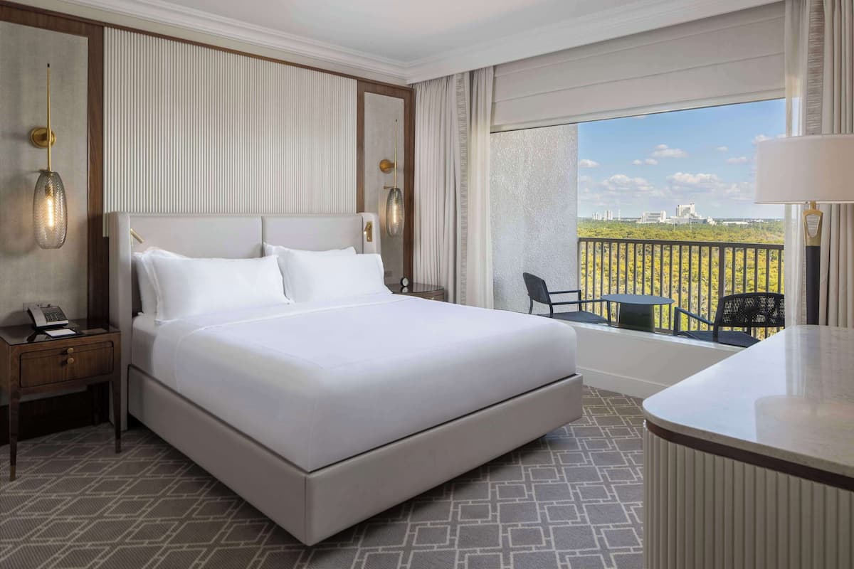 Une chambre d’hôtel avec un grand lit, un bureau avec une lampe, une chaise et un balcon donnant sur la ville.