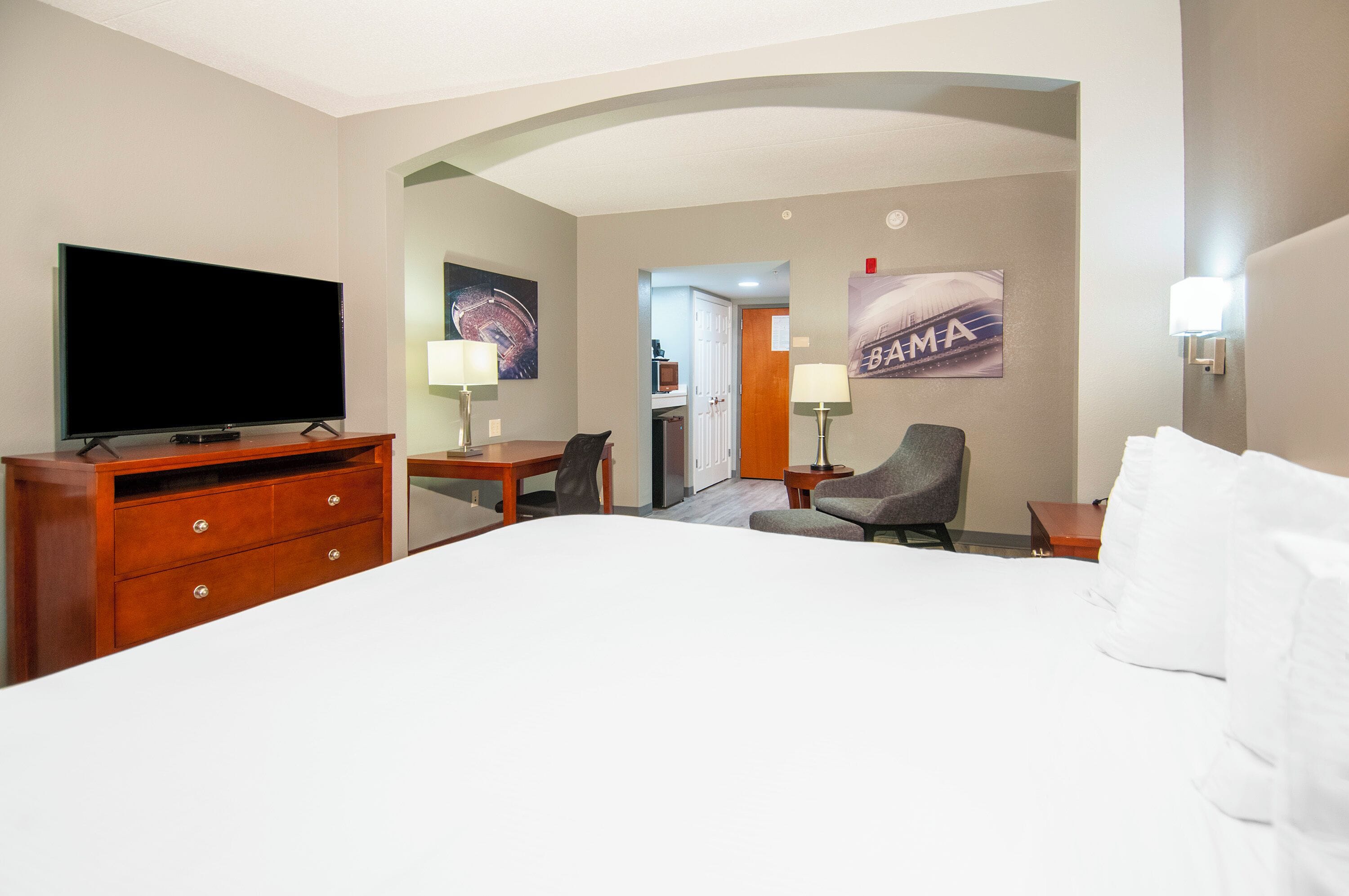 A hotel room with a large bed, a flat-screen TV, a desk with a chair, a lamp, and a painting on the wall.