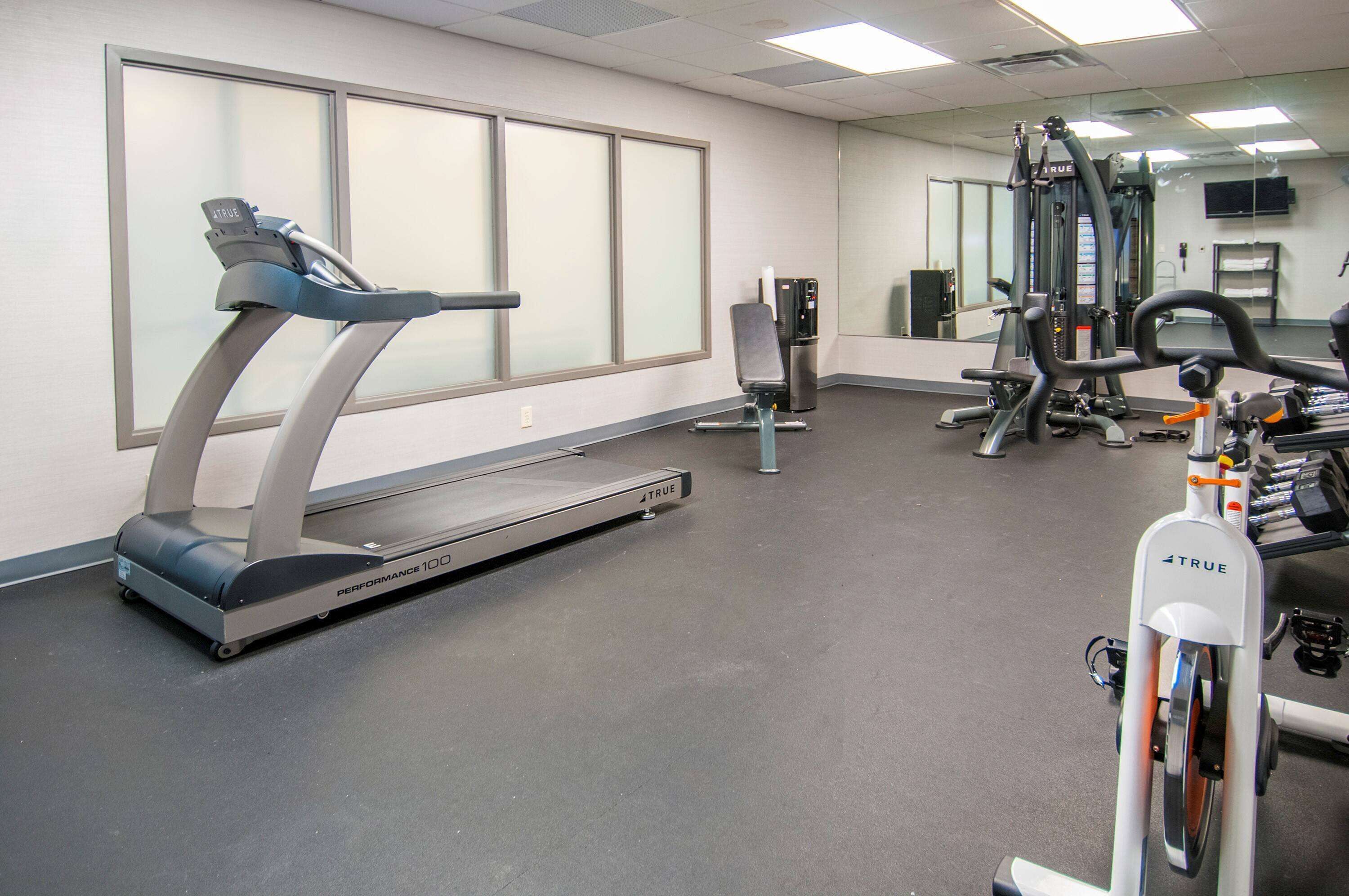 A gym with a treadmill, weight machines, and a mirror.