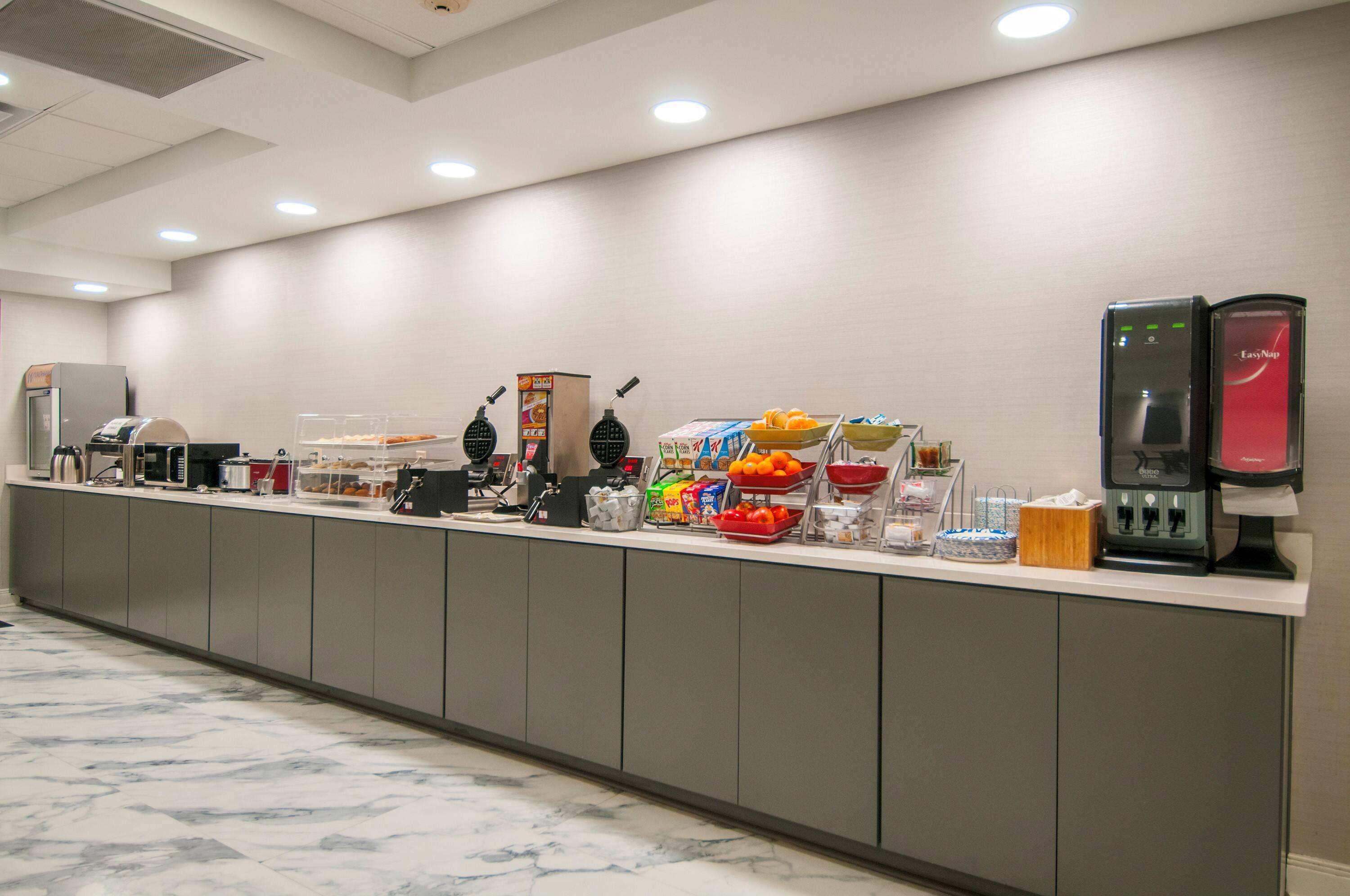 A self-service breakfast bar with various food items and beverages, a coffee machine, and a digital scale.