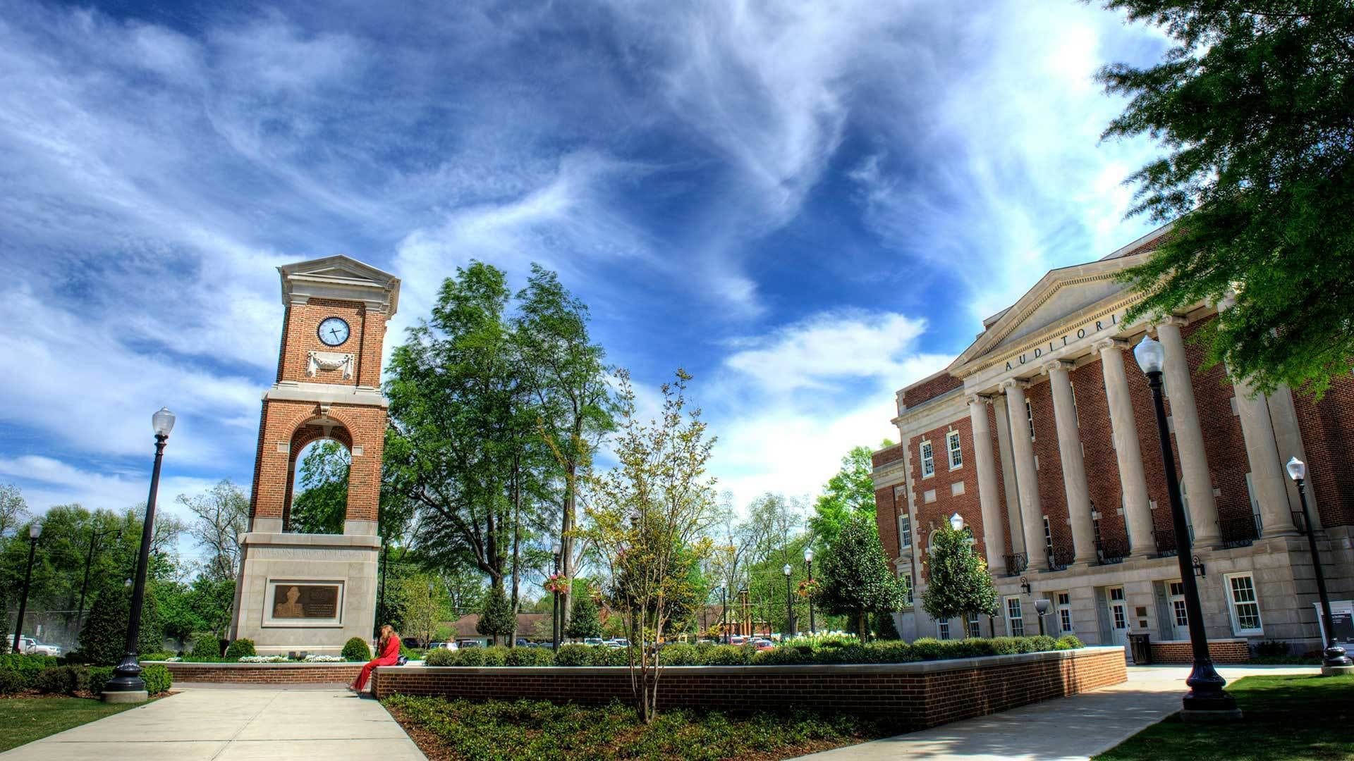 A university campus with a clock tower, a large building labeled 'AUDITORIUM', and a well-maintained lawn area.