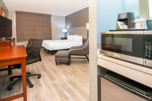A hotel room with a bed, a desk, a chair, a microwave, and a coffee maker.