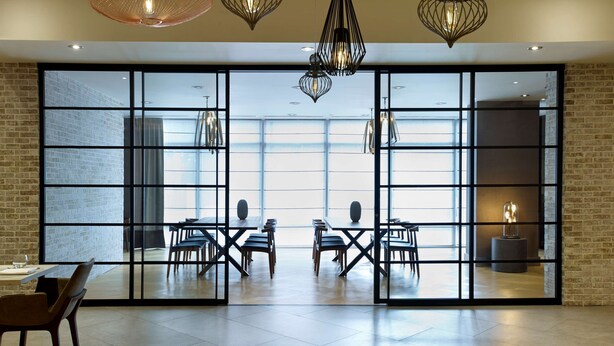 A spacious room with a large glass wall, a wooden floor, and a dining area with tables and chairs. - Hilton Garden Inn Toronto Airport (Mississauga)