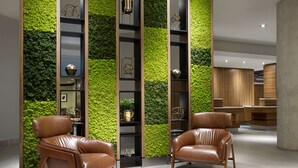 A modern interior with two leather chairs, a green vertical garden wall, and wooden shelving units. - Hilton Garden Inn Toronto Airport (Mississauga)