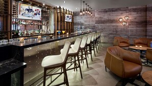 A bar area with a long counter, multiple stools, and a seating area with leather chairs. - Hilton Garden Inn Toronto Airport (Mississauga)