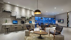 A modern hotel lobby with a brick wall, bar area, seating, and large windows. - Hilton Garden Inn Toronto Airport (Mississauga)