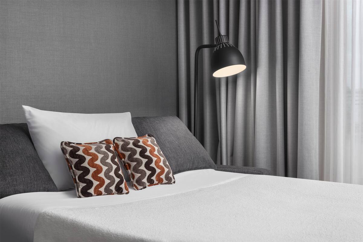 A neatly made bed with white linens, two pillows, and a black floor lamp.