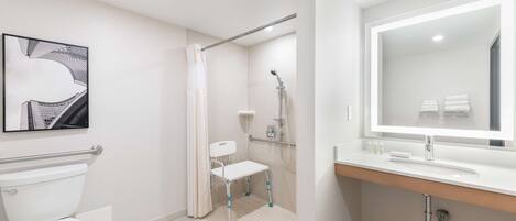 A modern bathroom with a toilet, a shower with a grab bar, a sink with a mirror, and a framed picture on the wall.
