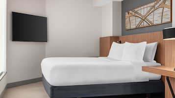 A modern hotel room with a bed, a flat-screen TV mounted on the wall, and a decorative wall piece above the bed.