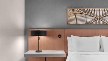 A hotel room with a wooden headboard, a bedside table with a lamp, and a painting above the bed.