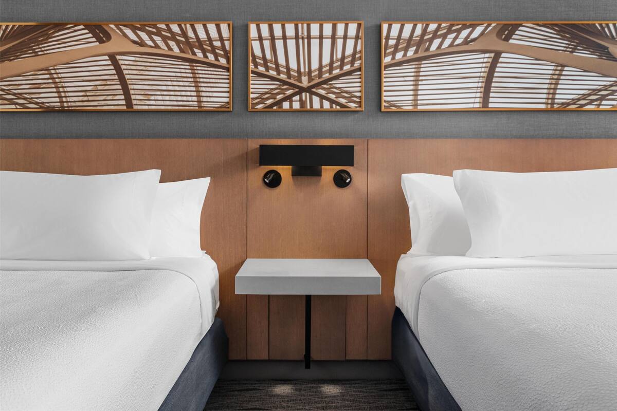 A hotel room with two beds, a small table, and a wooden ceiling design.