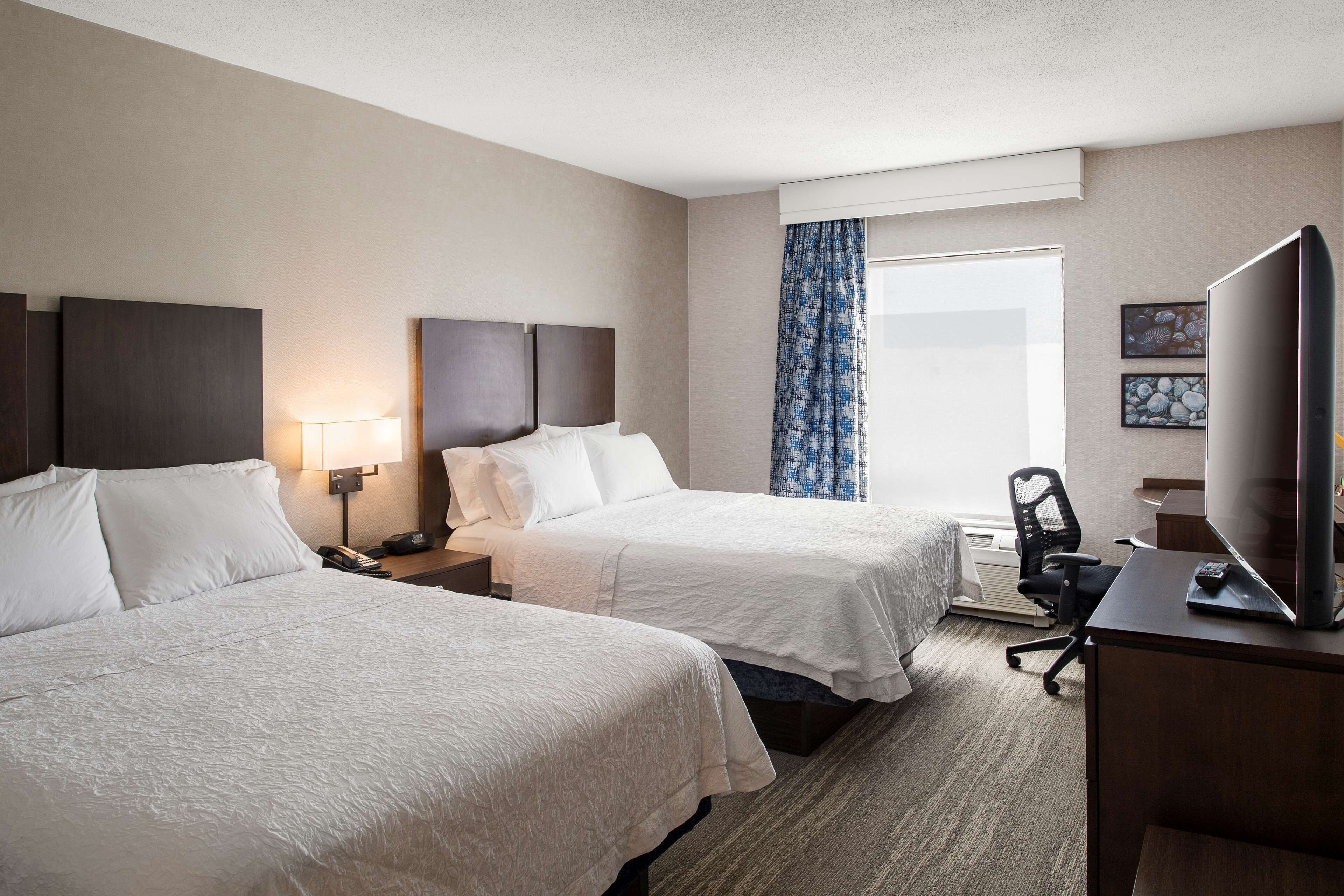 A hotel room with two beds, a desk with a TV, a chair, and a window with curtains.