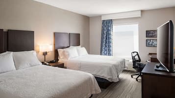 A hotel room with two beds, a desk with a TV, a chair, and a window with curtains.