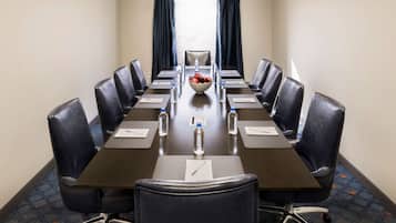 A conference room with a long table, chairs, water bottles, and a bowl of fruit.