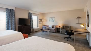 A hotel room with two beds, a TV, a desk with a lamp, a chair, a sofa, and a small table.