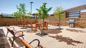 An outdoor patio area with brick flooring, wooden furniture, and a barbecue grill. - Hampton Inn & Suites by Hilton Halifax - Dartmouth (Dartmouth)